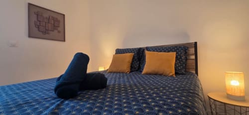Chambre cosy de l'hôtel NN Patrimoine à Douvaine avec lit à motifs bleus, coussins dorés, lumière chaleureuse et décoration murale