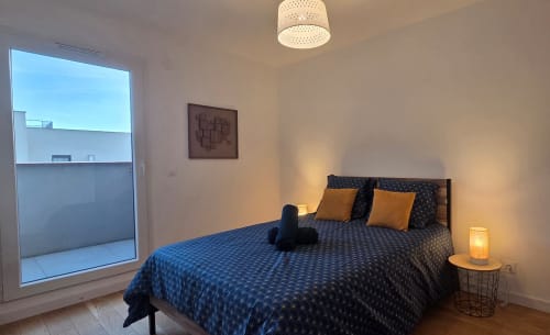 Chambre moderne de l'appartement L'Idéal à Douvaine chez NN Patrimoine avec lit motifs bleus, coussins oranges et vue balcon