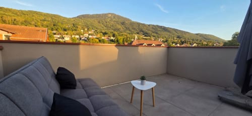Terrasse panoramique NN Patrimoine à Douvaine avec canapé gris, table d'appoint et vue sur les montagnes boisées
