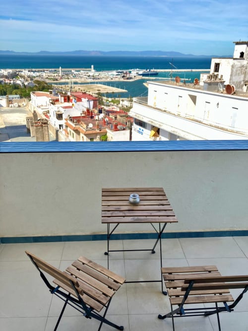Terrasse sur toit à Tanger avec chaises en bois, table et vues panoramiques sur la baie