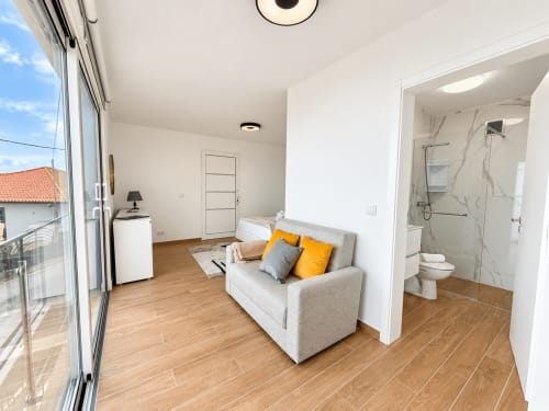 Modern studio at Check Madeira, Ribeira Brava with beige sofa, wooden floors, ensuite bathroom, and balcony views