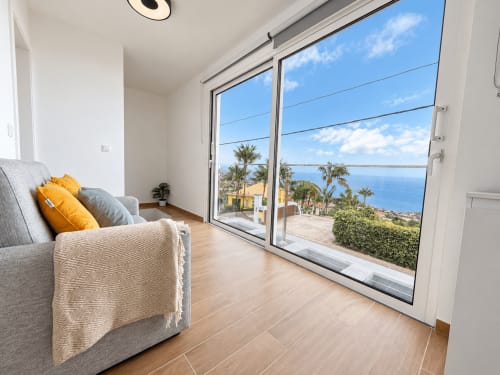 Modern bedroom at Check Madeira in Ribeira Brava with ocean views, gray armchair, wooden floors, and sea-facing balcony.