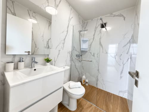 Modern bathroom at Check Madeira hotel in Ribeira Brava with marble-patterned walls, walk-in shower, white vanity and wood