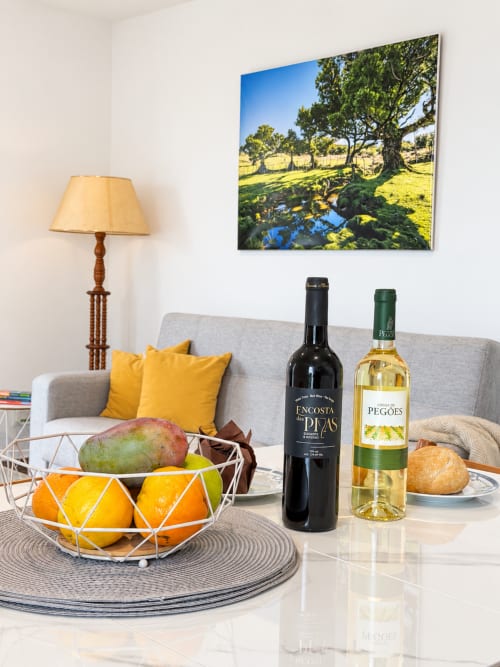 Elegant living room at Check Madeira with fruit bowl, wine bottles, lamp, and landscape artwork overlooking Ribeira Brava