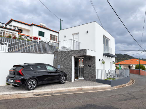 Check Madeira hotel exterior in Ribeira Brava with modern white building, black car parked, and cloudy sky