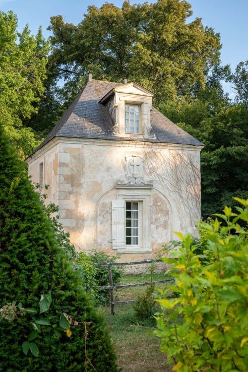 Stone chapel at Château De Chambiers with mansard roof, surrounded by lush greenery and garden gate in Durtal, France