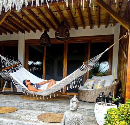 Relaxation area at Malù Surf Boutique Hotel in Canoa with hammock, woven seating, wooden beams, and Buddha statue