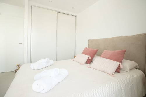 Dormitorio moderno en Villa MERAKI, Corralejo Fuerteventura, con cabecero beige, almohadas rosas y toallas blancas enrolladas en la cama