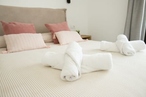Dormitorio lujoso en Villa MERAKI, Gozamena Corralejo, con toallas blancas enrolladas en la cama y almohadas rosa