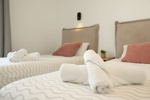 Camas gemelas con sábanas blancas, almohadas coral y toallas enrolladas en la Villa MERAKI de Gozamena, Fuerteventura