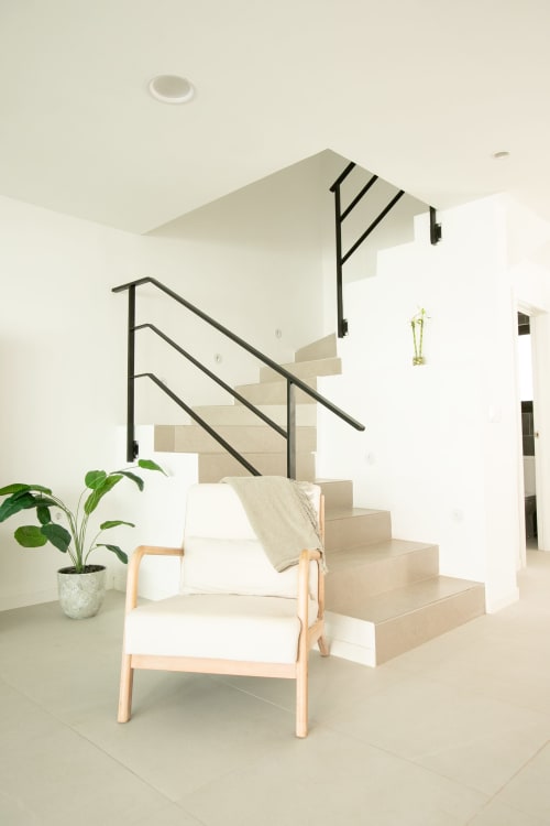Escalera moderna de villa con barandillas de metal negro, escalones de madera, paredes blancas, planta en maceta y silla contemporánea en Gozamena