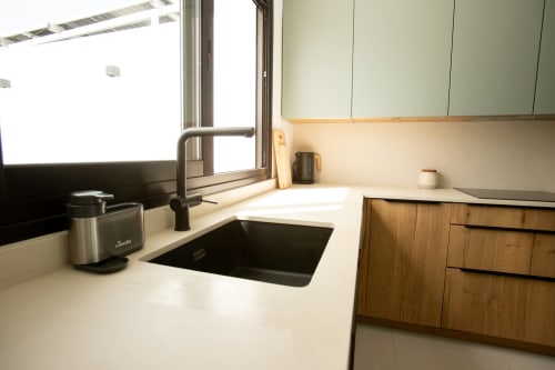 Moderna cocina de villa con fregadero negro, grifo acero inoxidable, encimeras blancas, muebles madera y vista a ventana en Gozamena