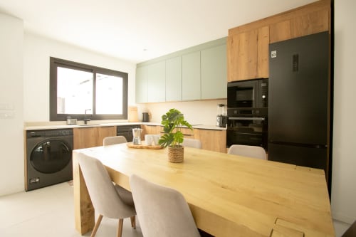 Moderna cocina-comedor en Villa MERAKI con mesa de madera, sillas color crema, electrodomésticos negros y muebles verdes