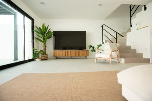 Sala de estar de villa moderna con televisor de pantalla plana, mueble de madera para medios, sillón crema, plantas en maceta y acceso a escaleras