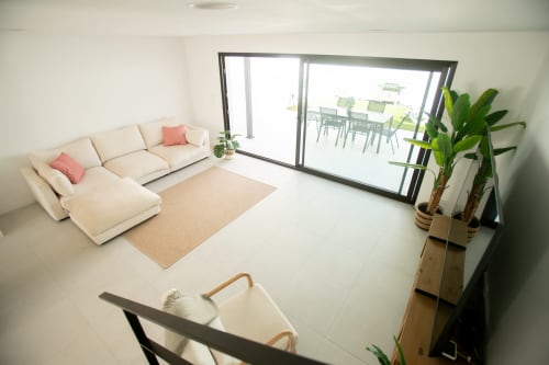 Elegante sala de Villa MERAKI en Corralejo con sofá seccional color crema, vistas al mar por puertas correderas y plantas decorativas