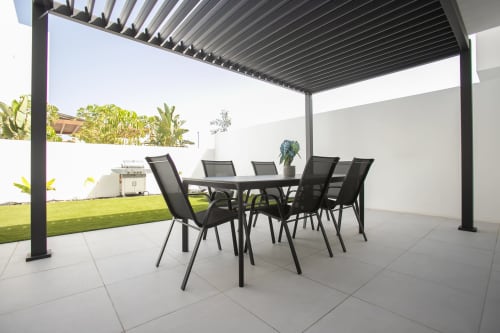 Zona de comedor al aire libre moderna en Villa MERAKI de Corralejo, Fuerteventura con mesa negra, sillas y pérgola retráctil