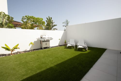 Patio de Villa MERAKI Fuerteventura con jardín cuidado, tumbonas, parrilla a gas y paredes blancas