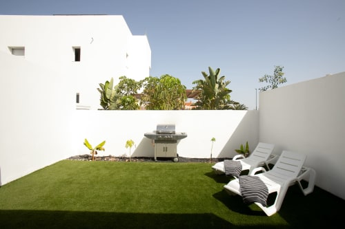 Jardín privado de Villa Meraki con césped, tumbonas, parrilla y muros blancos en Corralejo, Fuerteventura