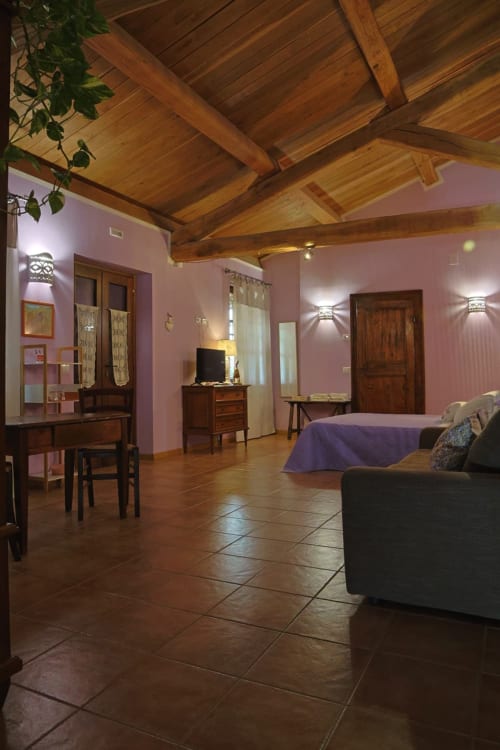 Ampia camera da letto presso La Casa dei Tigli B&B a Cannara con travi in legno a vista, pareti rosa e pavimenti in cotto