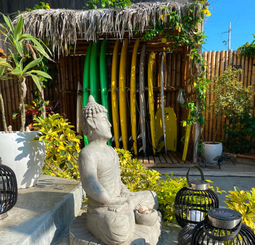 Buddha statue in tropical garden courtyard at Malù Surf Boutique Hotel in Canoa, Ecuador, with surfboards and palapa roof