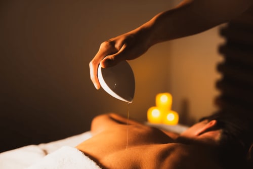 Massage oil dripping onto a guest's back at Malù Surf Boutique Hotel spa in Canoa with candlelight ambiance