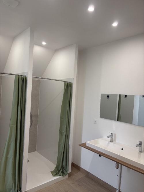 Salle de bains commune moderne au Domaine Du Grand Fort avec vasques doubles, grand miroir, rideaux de douche verts et éclairage encastré