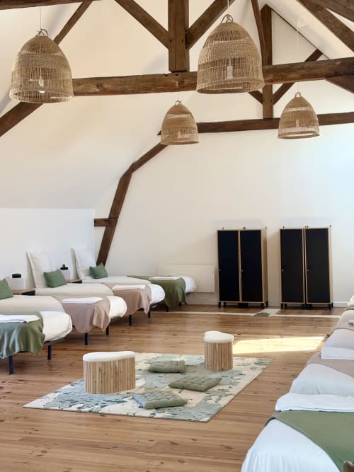 Dortoir spacieux du Domaine Du Grand Fort avec 14 lits, poutres en bois apparentes, luminaires suspendus tissés et salle de bains commune