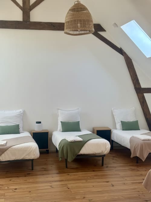 Chambre lumineuse au Domaine Du Grand Fort avec trois lits simples, accents verts, parquet et poutres apparentes