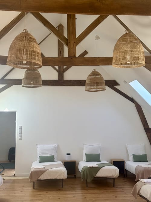 Chambre de dortoir spacieuse avec quatre lits simples, suspensions en rotin, poutres apparentes et murs blancs au Domaine Du