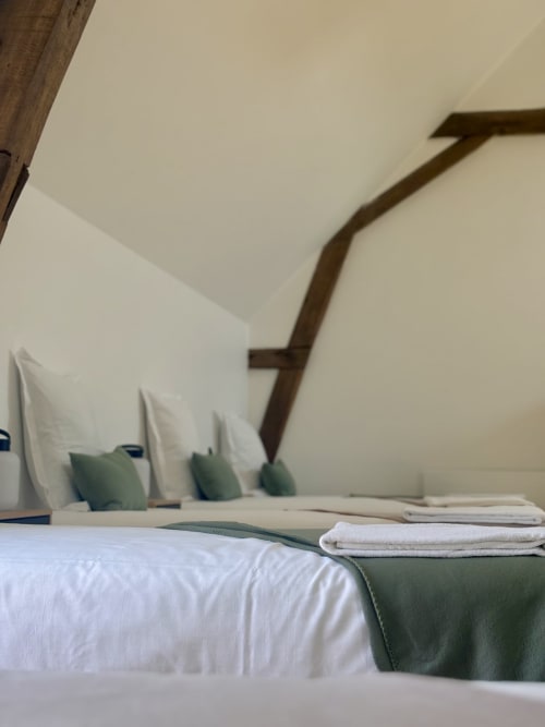 Chambre cosy du gîte Domaine Du Grand Fort avec literie blanche, accents vert sauge, poutre en bois et serviettes soigneusement disposées