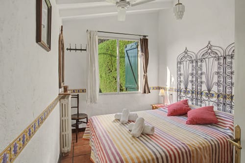 Dormitorio luminoso en el B&B Can Gat Vell de Girona con ropa de cama a rayas, cabecero de metal ornamentado y vistas al jardín
