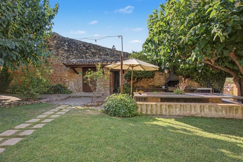 Patio de Can Gat Vell con edificio de piedra, sombrilla, césped e hiedra trepadora en Girona, Empordà