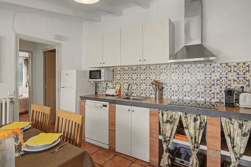 Cocina moderna con armarios blancos, salpicadero de azulejos y zona de comedor en la casa rural Can Gat Vell en Cataluña