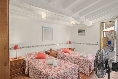 Dormitorio doble con edredones rojo estampado, muebles de madera y vigas blancas vistas en la casa rural Can Gat Vell en Saus, España