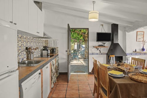 Cocina y comedor rústicos de estilo español con armarios blancos, azulejos decorativos y vistas al jardín