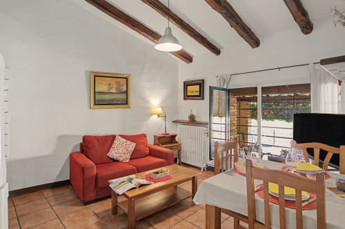 Acogedora sala de estar de la casa rural con sofá rojo, vigas de madera y vistas al jardín en Can Gat Vell en Saus, España