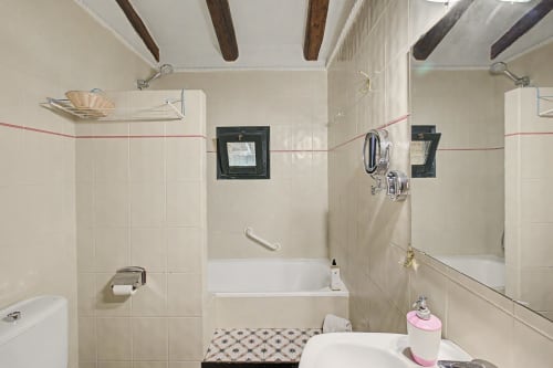 Baño de la casa rural Can Gat Vell en Saus con paredes alicatadas, accesorios blancos, doble lavabo y vigas de madera vista