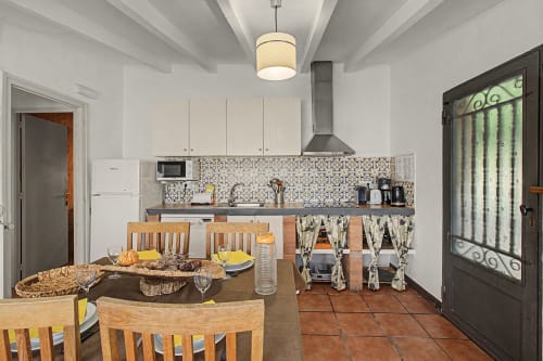 Cocina y comedor de una casa de campo española con armarios blancos, salpicadero de mosaico, sillas de madera y azulejos de barro