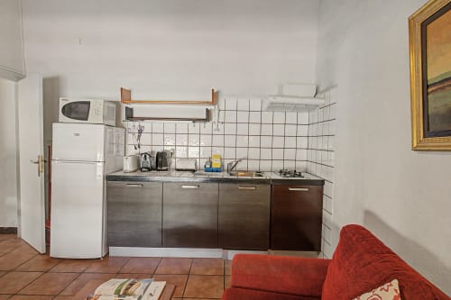 Área de cocina en la casa rural Can Gat Vell con nevera, microondas, cocina de gas y azulejos blancos en la pared