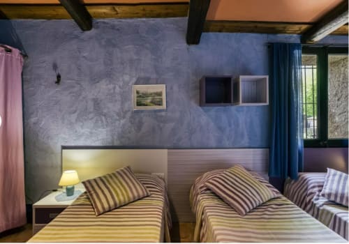 Dormitorio rústico en una masía catalana del siglo XVIII con ropa de cama a rayas, vigas vistas y paredes lavanda en Can Gat Vell