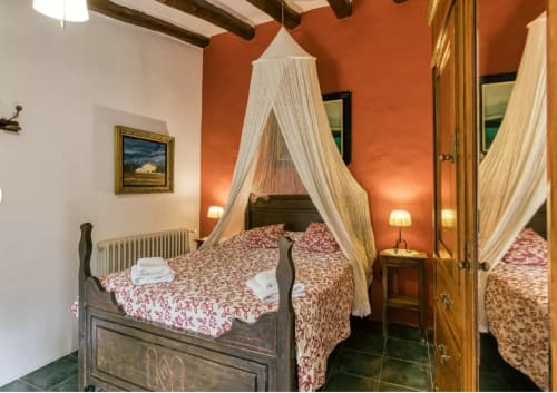 Dormitorio rústico con cama con dosel, ropa de cama roja estampada y vigas de madera vista en Can Gat Vell, Saus, Cataluña