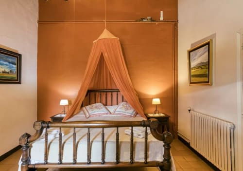 Dormitorio rústico con cama con dosel naranja, marco metálico, dos lámparas y paredes color terracota en la casa rural Can Gat Vell de Cataluña