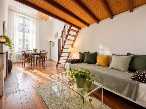 Suite lumineuse en mezzanine à Au Bon Gîte à Senones avec poutres apparentes, canapé, coin repas et escalier en bois vers la mezzanine