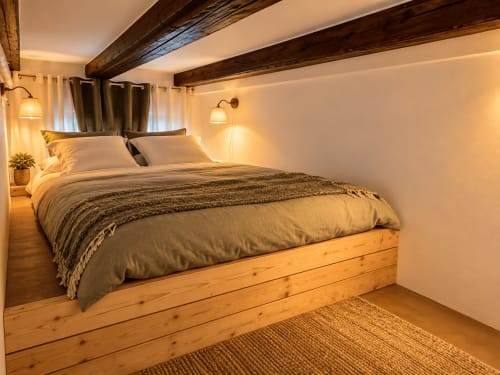 Chambre en mezzanine de la Suite Rustique à Au Bon Gîte avec poutres en bois, lumière chaleureuse et sol en bois