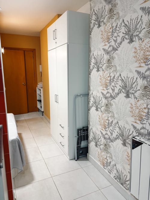 Cocina moderna en apartamento La Ventana, Costa Brava, con muebles blancos, papel tapiz botánico y piso de baldosas beige