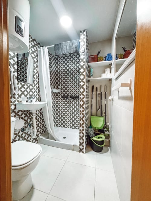 Baño moderno en apartamento La Ventana, Costa Brava, con ducha de azulejos geométricos, lavabo blanco, inodoro y estantes de almacenaje