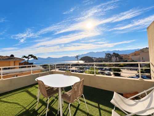Terrasse ensoleillée vue mer d'un T3 à L'Île-Rousse, Corse. Table à manger blanche, chaises, hamac et Méditerranée