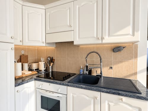Cuisine moderne avec armoires blanches, comptoirs en granit noir, dosseret en carrelage beige et appareils en acier inoxydable