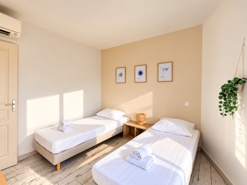 Chambre double lumineuse de l'appartement L'Île-Rousse avec deux lits, murs beiges et lumière naturelle