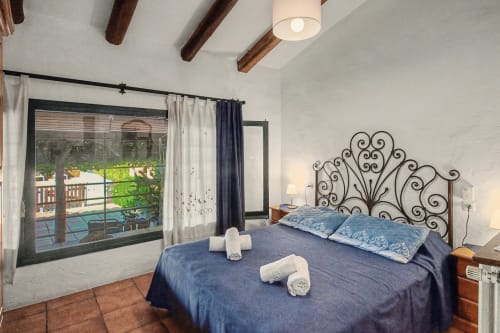 Dormitorio con cabecero de hierro forjado ornamental, ropa de cama azul, vigas de madera, vista a la piscina en cottage Can Gat Vell